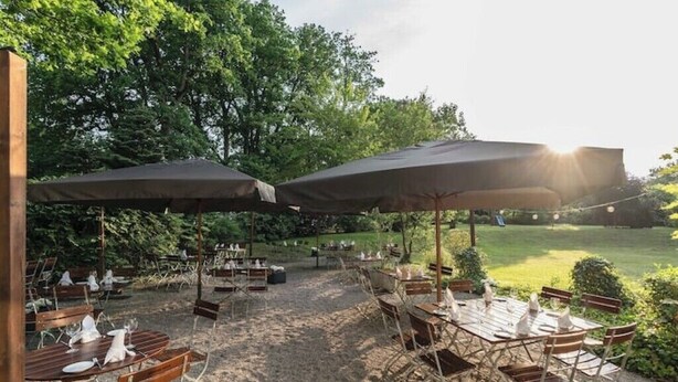 An outdoor dining area with tables and chairs, covered by large umbrellas, set on a gravel surface with trees in the background. - Apartment in Buchholz in der Nordheide, Germany (Buchholz in der Nordheide)