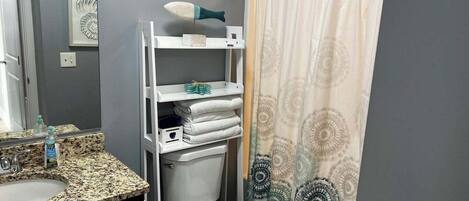 Un baño con encimera de granito, inodoro blanco, estante con toallas y cortina de ducha con diseño circular.