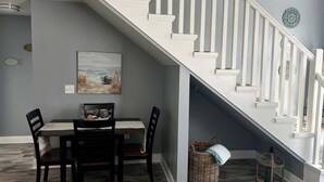 Un comedor con una mesa y sillas, una escalera con barandillas blancas y un cuadro en la pared.