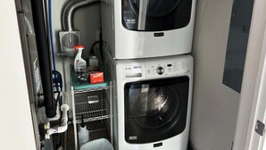 Un área de lavandería compacta con dos lavadoras apiladas, un calentador de agua y una manguera.