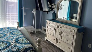 Un dormitorio con cama, cómoda, televisor y ventana con cortinas.