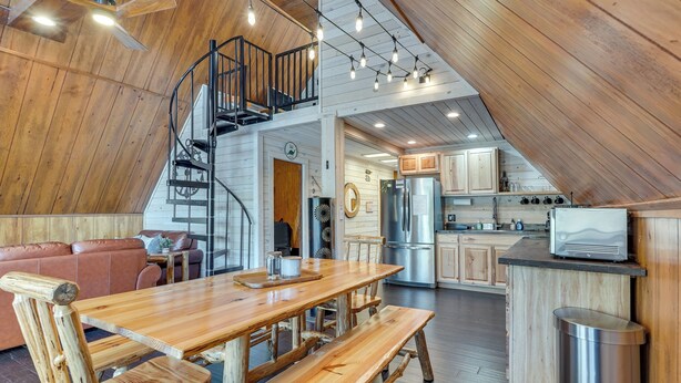 Un loft spacieux comprenant une table à manger en bois, des bancs, un escalier et un coin cuisine.
