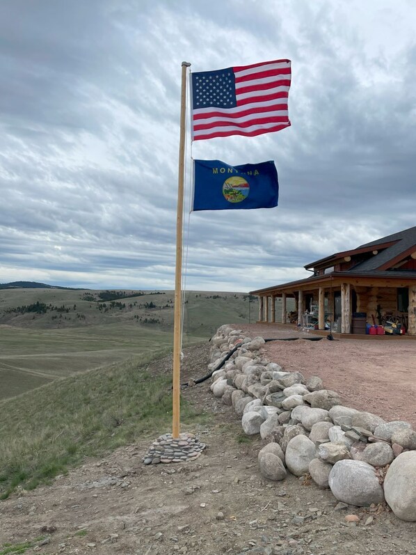 Ein Fahnenmast mit der US-amerikanischen Flagge und der Landesflagge von Montana, eine Steinsäule und ein Gebäude mit einer Veranda.