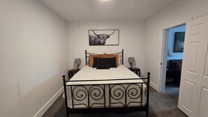 A bedroom with a bed, two bedside tables, a wall-mounted picture, and a door leading to another room. - Midtown Condo right on Main St! Walking distance to everything! (Lava Hot Springs)