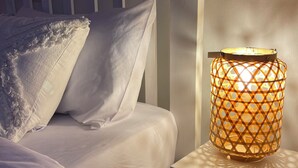 Una cama con ropa de cama y almohadas blancas, un cabecero de madera y una mesita de noche con una lámpara.