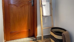 Una puerta de madera con un tirador metálico, una escalera de madera apoyada en una pared y una cesta tejida sobre una alfombra a rayas.