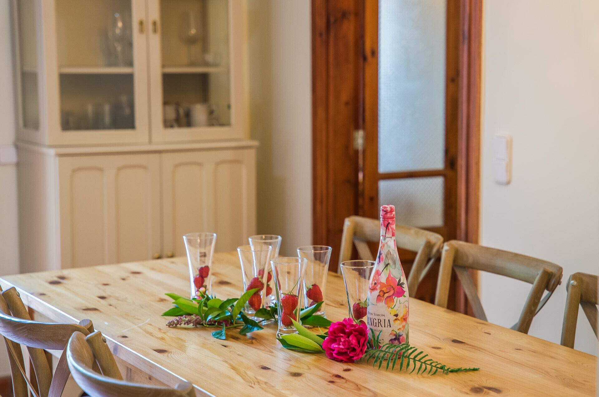 A wooden dining table with clear glassware, a bottle, and decorative flowers.