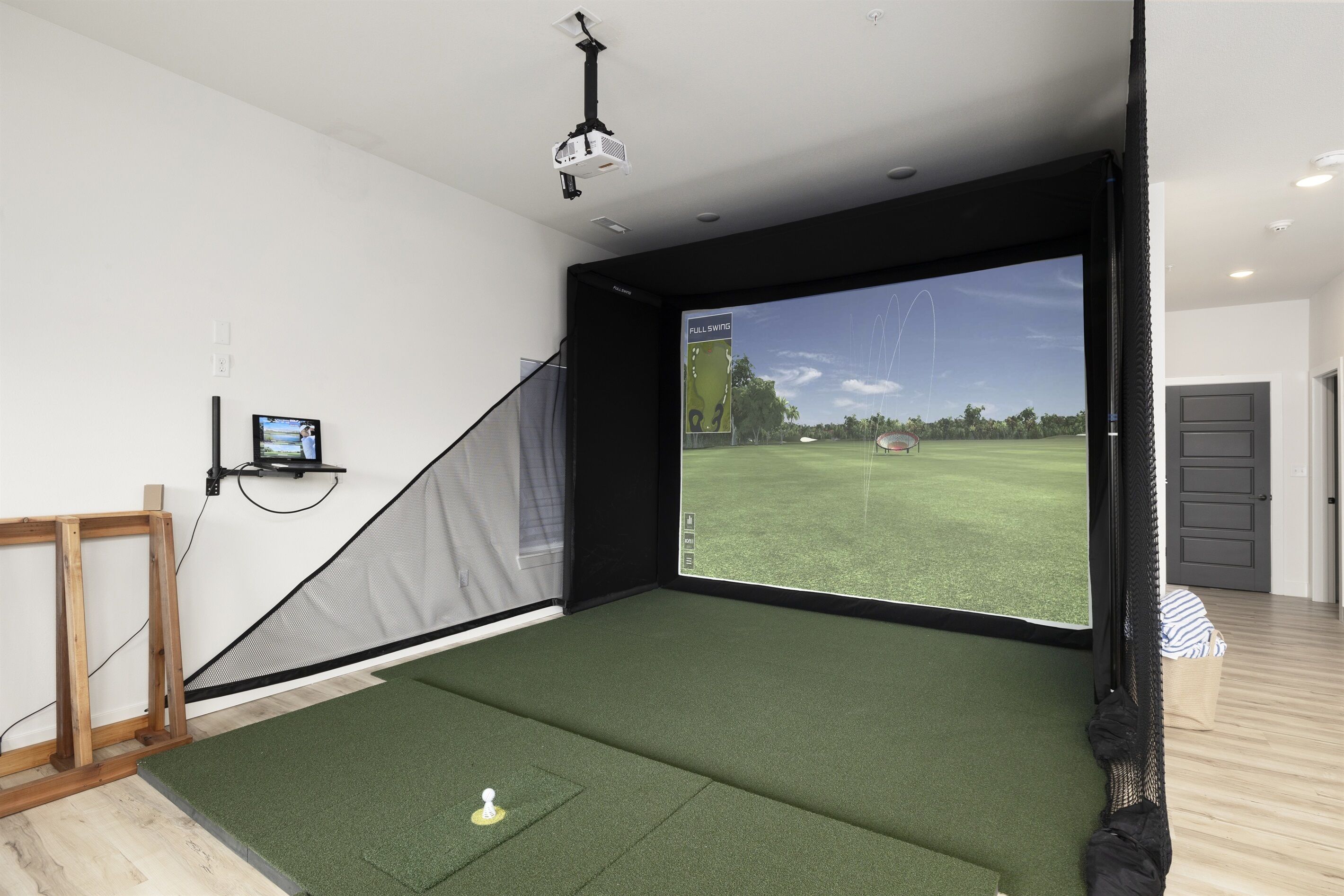 Una habitación con una pantalla grande que muestra un campo de golf, un proyector y una red de práctica de golf.