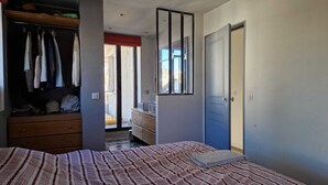 Ein Schlafzimmer mit Bett, Schrank, Badezimmer und einer Schiebetür zum Balkon.