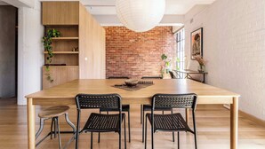 A dining area with a wooden table, black chairs, a hanging light fixture, and a brick wall.