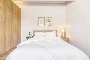 A neatly made bed with white linens, a wooden wardrobe, a bedside table with a lamp, and two framed pictures on the wall. - Unwrap history at Charlie’s Chocolate Factory (Fitzroy)