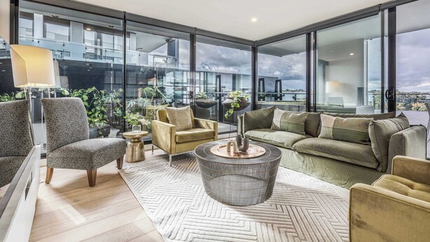 Una sala de estar moderna con un sofá, sillones, una mesa de centro y ventanas amplias que ofrecen vistas a la ciudad.