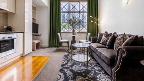 Ett kompakt bostadsutrymme med ett litet kök, en soffa, ett soffbord och utsikt genom ett fönster.