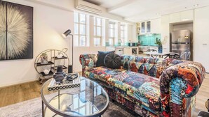 A modern living room with a colorful sofa, a glass coffee table, and a kitchen in the background. - Vintage glamour with indoor pool in heritage CBD (Melbourne)
