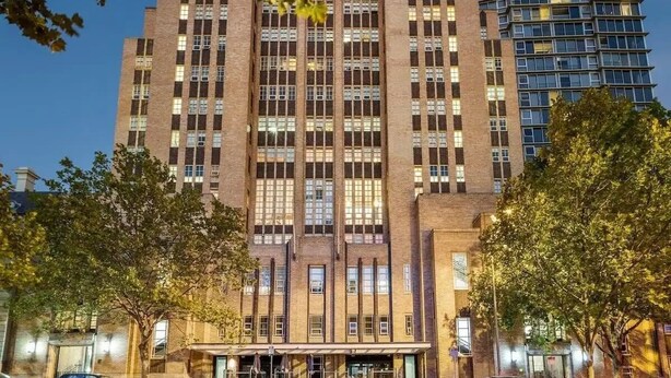 A multi-story building with a central entrance, large windows, and a parking area in front. - Vintage glamour with indoor pool in heritage CBD (Melbourne)
