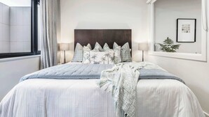 Un dormitorio moderno con una cama grande, un cabecero oscuro y una ventana con cortinas.
