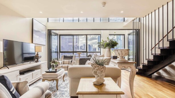 A spacious living room with a large TV, comfortable seating, a staircase, and a city view.