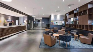 A modern hotel lobby with a reception desk, seating area, and a bar.