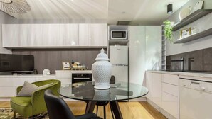 A modern kitchen with white cabinets, a glass dining table, a green chair, and a white vase.