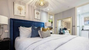 A modern hotel room with a large bed, a nightstand, a lamp, and framed artwork on the walls.