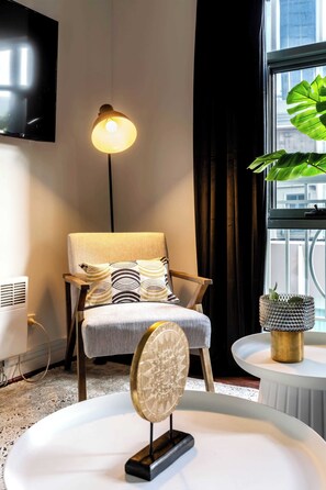 A modern living room with a sofa, a standing lamp, a TV mounted on the wall, and a large window with a view of buildings. - Leafy CBD oasis steps from Southern Cross Station (Melbourne)