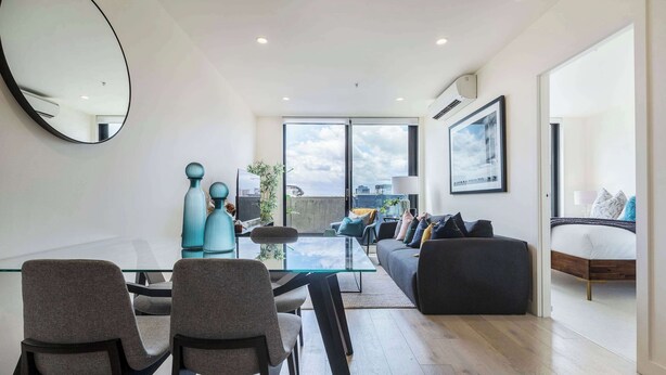 Ein modernes Wohnzimmer mit einem Glastisch, grauen Sesseln, einer Couch und einem großen Fenster mit Blick auf die Stadt.