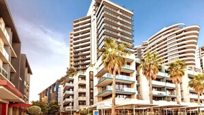 Un hotel moderno con varios edificios altos, balcones y un patio central con palmeras.