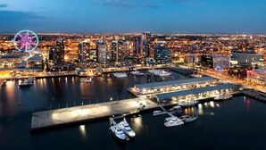 Un paisaje urbano con un puerto deportivo frente al mar, una noria grande y edificios modernos.