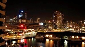 Un paisaje urbano nocturno con edificios iluminados y un puerto deportivo con barcos.