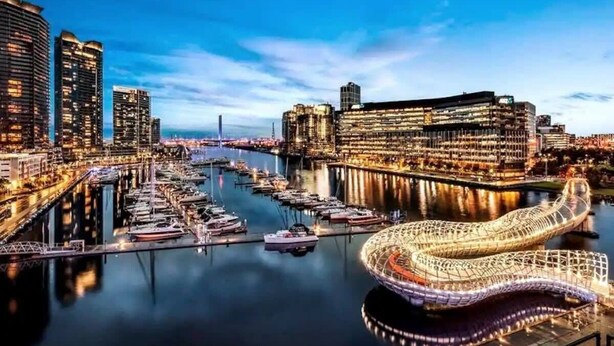 Un puerto deportivo con barcos, una estructura iluminada de gran tamaño y edificios altos.