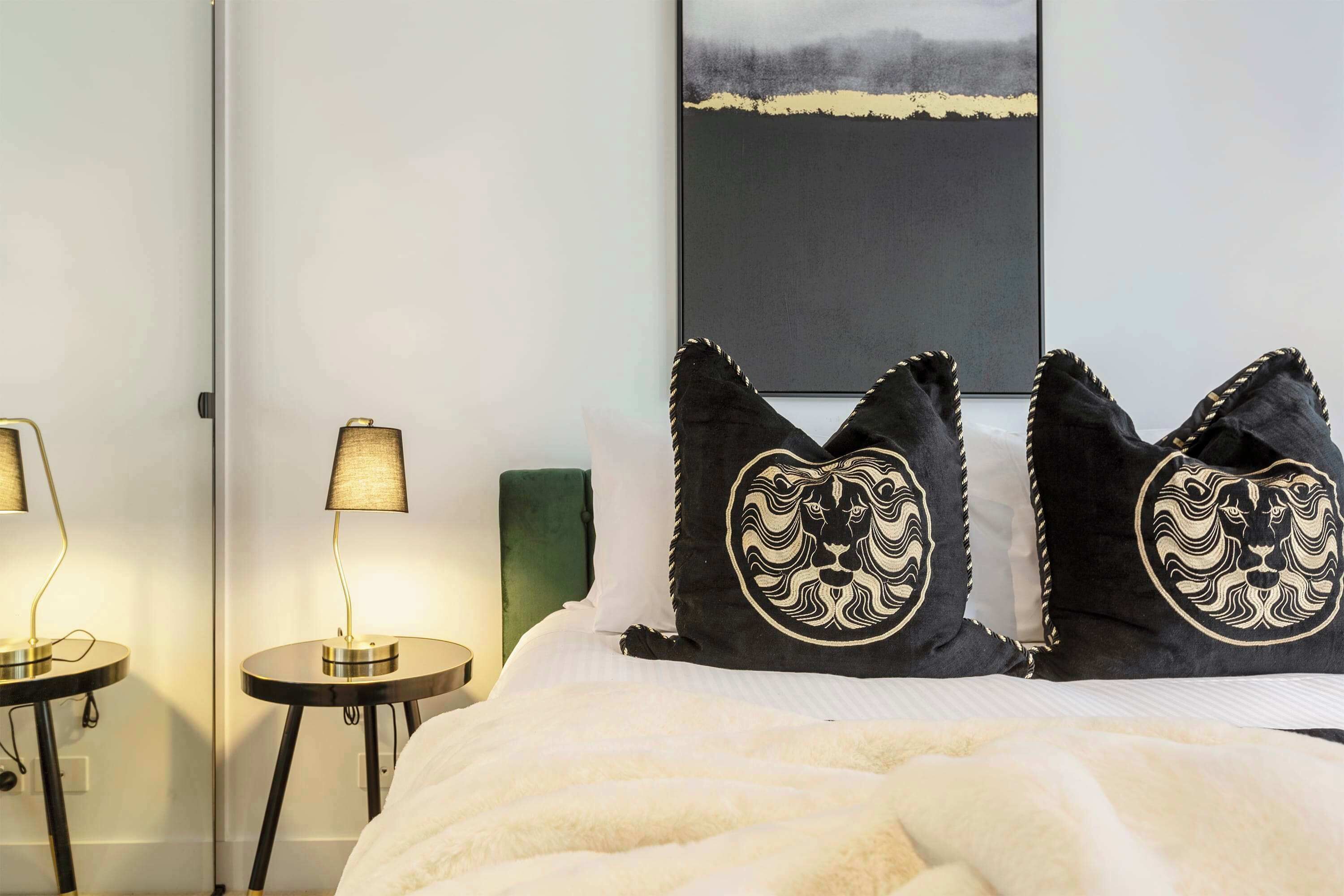 A hotel room with a bed, two bedside lamps, a green headboard, and a large abstract painting on the wall.