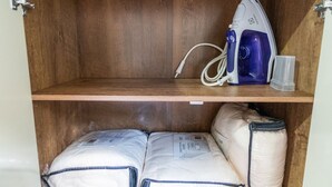 A wooden shelf with an iron and a plastic cup. Below, there are two bags of bedding.