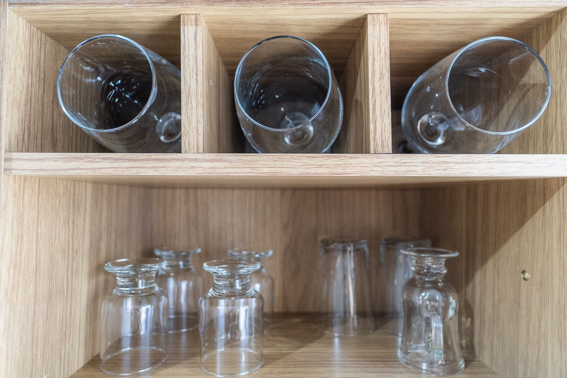 Un meuble en bois avec trois verres transparents sur l’étagère supérieure et plusieurs bouteilles transparentes sur l’étagère inférieure.