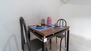 A small dining table with two chairs, a pink thermos, and two cups on a blue placemat.