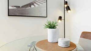 A modern dining area with a glass table, a potted plant, and a stack of white plates.