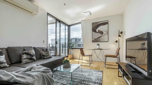 A modern living room with a sofa, coffee table, TV, and a large window offering a city view.
