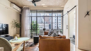 A modern living room with a leather sofa, a glass coffee table, a TV, and a large window with a city view. - Warehouse conversion in historic Dovers building (Melbourne)