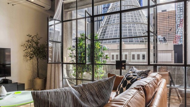 A modern living room with a leather sofa, a television, and a large window with a city view. - Warehouse conversion in historic Dovers building (Melbourne)
