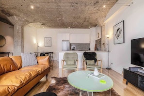 A modern living room with a leather sofa, two armchairs, a glass coffee table, and a kitchen in the background.