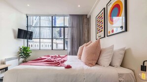 A hotel room with a large bed, a TV, a potted plant, and artwork on the walls. - Warehouse conversion in historic Dovers building (Melbourne)