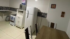 Une cuisine avec un réfrigérateur blanc, un four à micro-ondes et une bouilloire. On y trouve une table à manger avec des chaises. Les murs sont recouverts d’un revêtement mural noir et blanc à motifs.