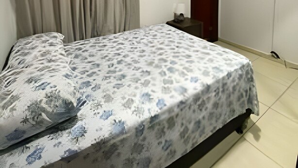 Une chambre à coucher avec un lit, des rideaux, un téléviseur fixé au mur et une porte.