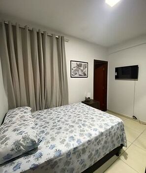 A bedroom with a bed, curtains, a wall-mounted TV, and a door.