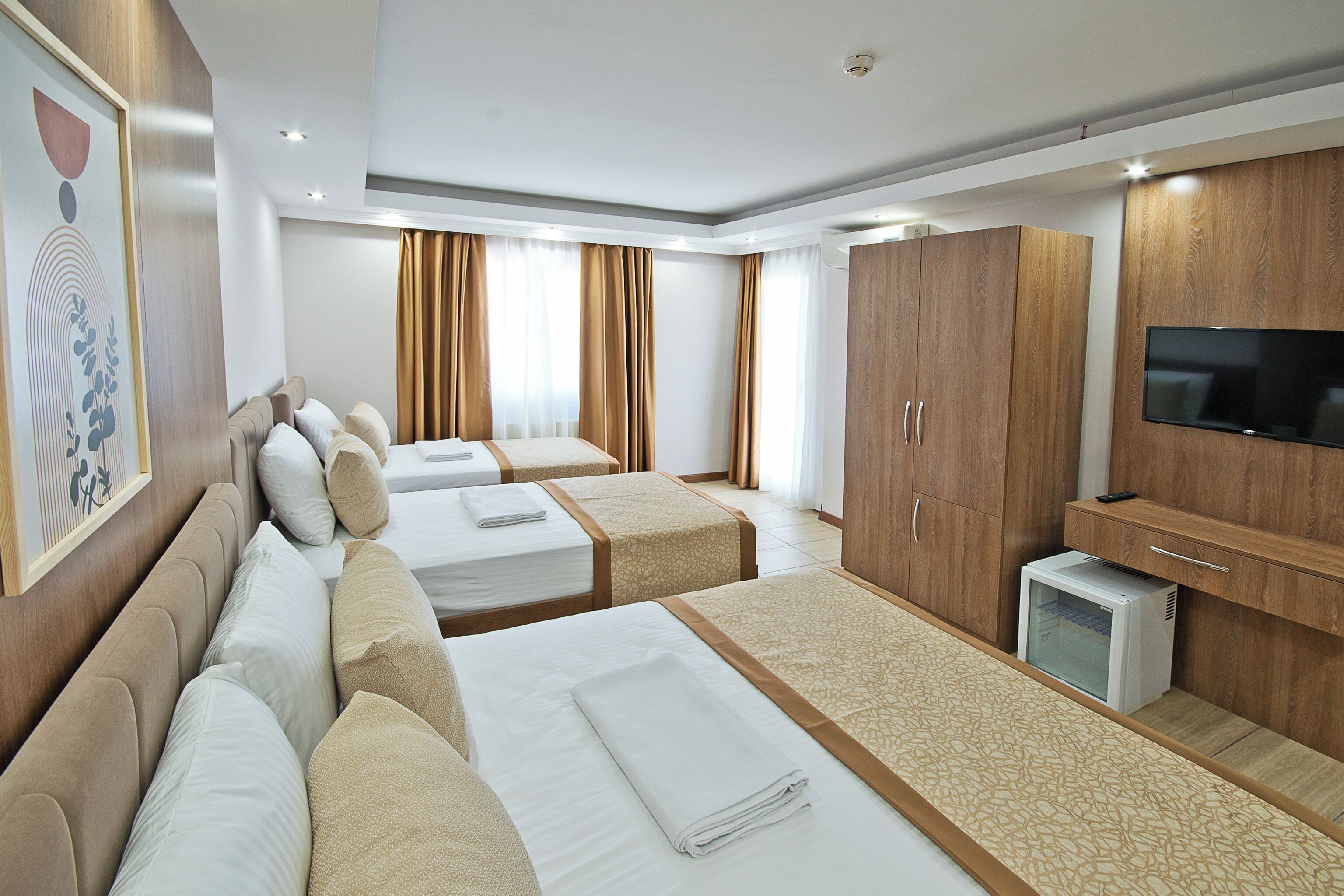 A hotel room with three beds, a TV, wooden wardrobe, and a painting on the wall.