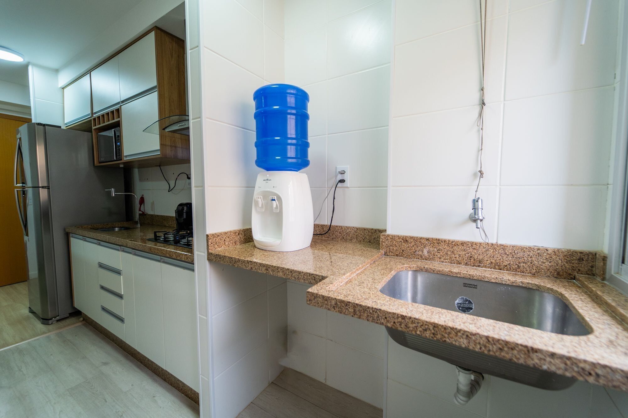 A kitchen with white cabinets, a granite countertop, a stainless steel sink, a water dispenser, and a microwave.