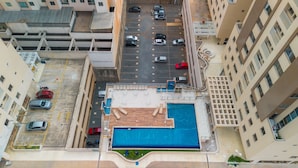 An aerial view of a parking lot with multiple cars, a swimming pool, and adjacent high-rise buildings. - Up to 5 Guests, Garage, Elevator, Swimming Pool, Jr Catito (Brasília)