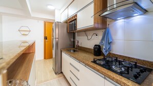 A modern kitchen with a stainless steel refrigerator, a microwave, a gas stove, and a built-in oven. There is a wooden door leading to another room, and a towel hanging on the wall. - Up to 5 Guests, Garage, Elevator, Swimming Pool, Jr Catito (Brasília)
