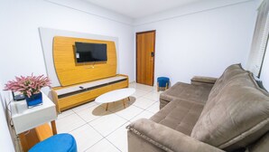 Een woonkamer met een flatscreen televisie bevestigd aan een houten wandmeubel, een bruine bank, een blauwe fauteuil en een klein wit tafeltje.