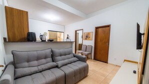 A living room with a grey sofa, a wooden cabinet, a coffee maker, and a television on a wooden stand. - Ap 73m2, 2 bedrooms with suite, Up to 6 Guests, 1G Wi-Fi, Jr Catito (Brasília)