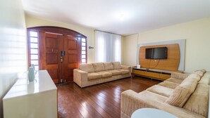A living room with a wooden floor, a sofa, a television mounted on the wall, and a door with a window.